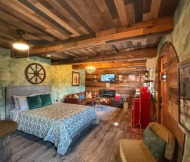 View of chair and bed with living room in the distance in Forest Hobbit-inspired cabin at Nature Mystique Retreat