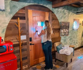 Woman looking through peekaboo window in front door of Forest Hobbit-inspired cabin at Nature Mystique Retreat.